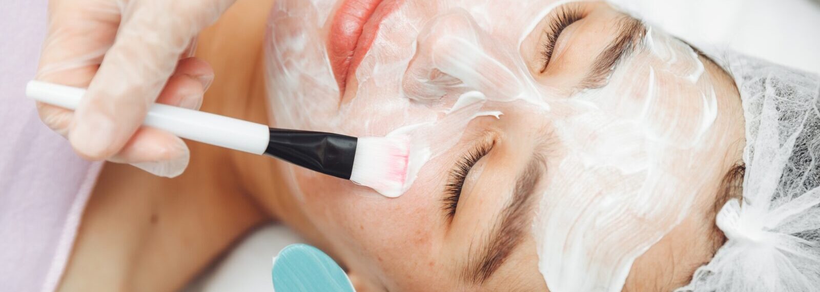 A cosmetologist does facial care and apply a face mask.